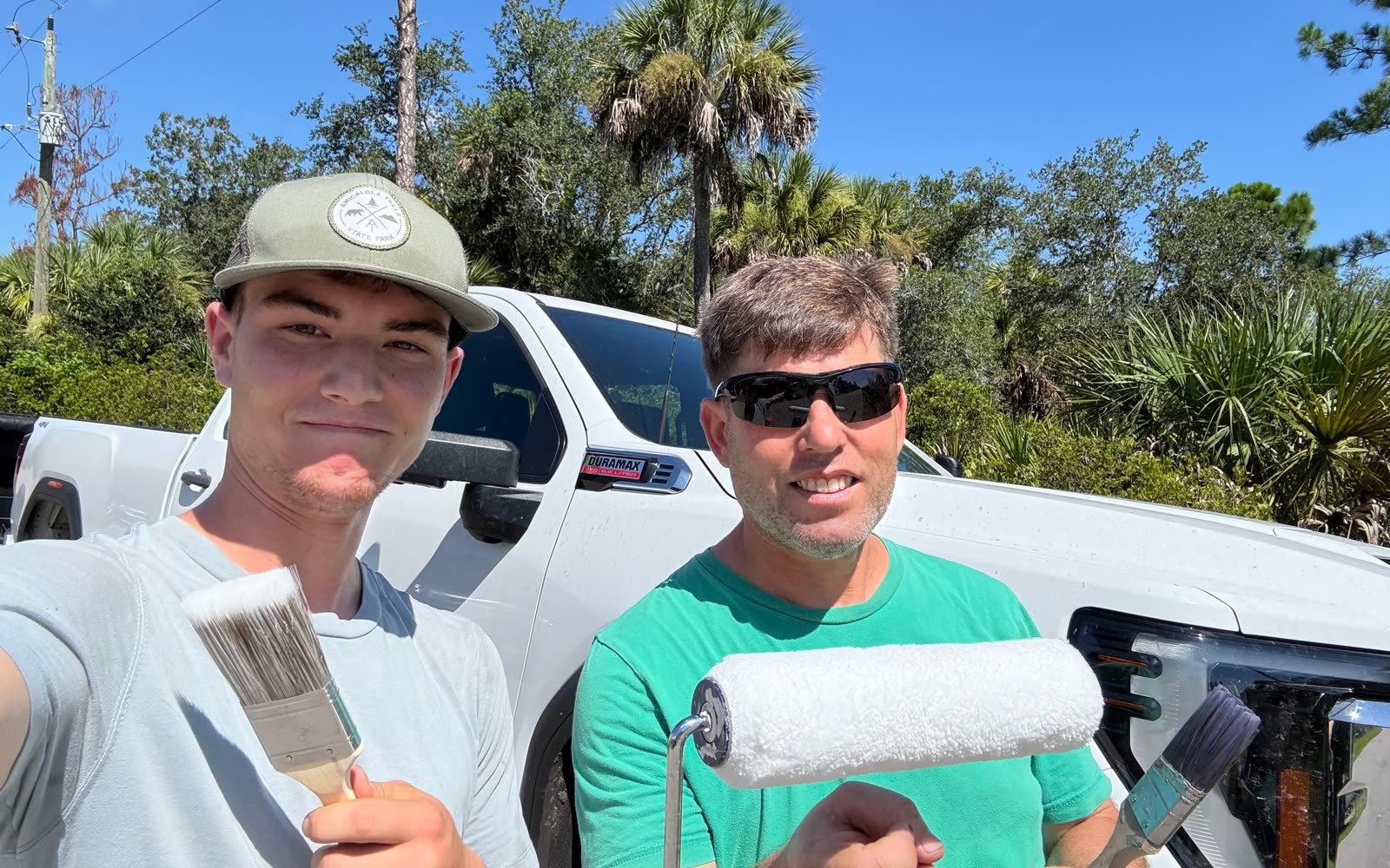 Vlad and Andrey, the owners of Port Charlotte House Painters, with a brush and roller in front of their work truck